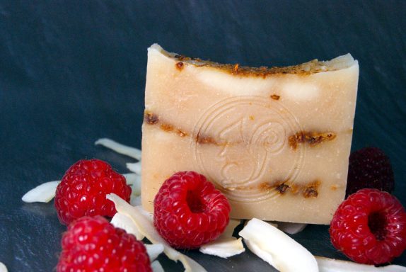 Handgemachte Seife mit Himbeeren und Kokosflocken auf einem dunklen Untergrund.