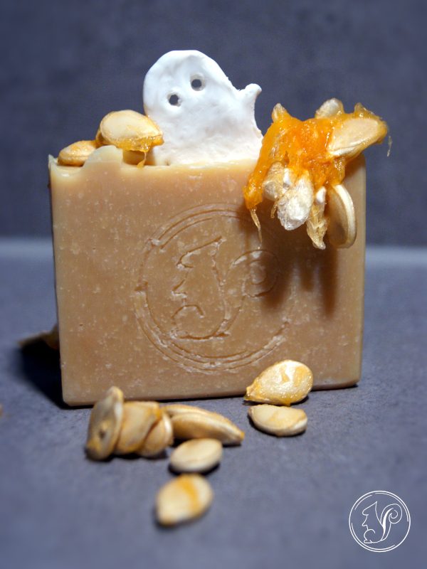 Seife mit Kürbiskernen und einer kleinen Geisterfigur, auf grauem Hintergrund.