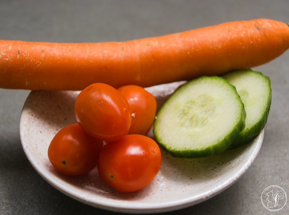Eine Karotte, Trauben-Tomaten und Gurkenscheiben auf einem weißen Teller.